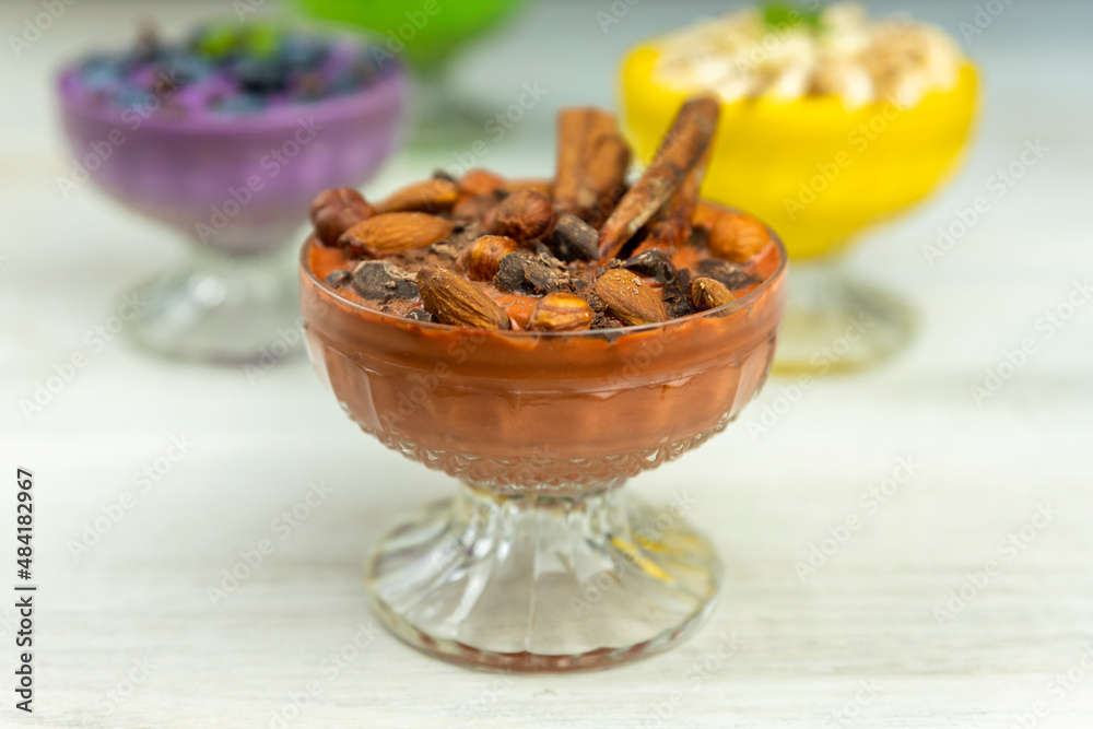 Smoothie or pudding with chocolate, hazelnuts and almonds served in a bowl for breakfast with several other smoothies in background