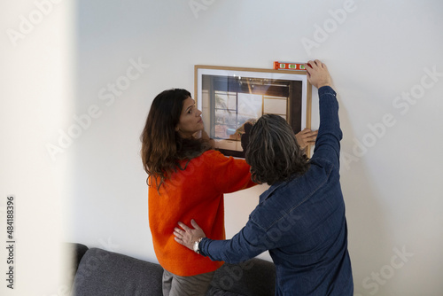 Heterosexual couple measuring level for hanging picture frame on wall while relocating in new house photo