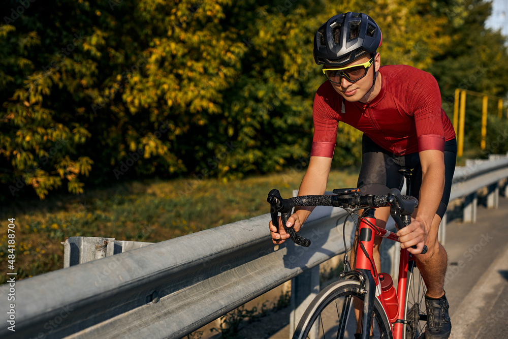Young caucasian cyclist in black helmet, protective glasses and active wear dynamically riding bicycle. Man preparing for competitions and races on fresh air. outdoors in nature, on road