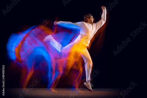 Stylish man in sports white suit dancing hip-hop isolated on dark background in mixed neon light. Youth culture, hip-hop, movement, style and fashion, action.