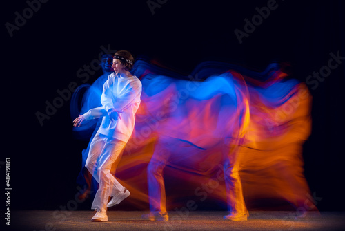 Stylish man in sports white suit dancing hip-hop isolated on dark background in mixed neon light. Youth culture, hip-hop, movement, style and fashion, action. © master1305