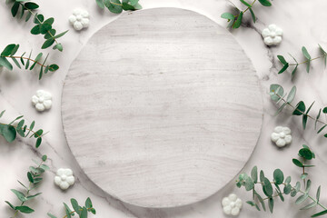 Wintertime mockup with copy-space on round, circle stone board. Fresh eucalyptus leaves and twigs. Top view on off white marble table. Winter flat lay background .