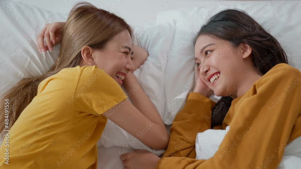Homosexual lesbian couple lying in bed with their heads close together. Woman and female share love, face each other, smile warmly at each other. Gay family. LGBTQ Pride Month, Couple Equality Concept Homosexual lesbian couple lying in bed with their heads close together. Woman and female share love, face each other, smile warmly at each other. Gay family. LGBTQ Pride Month, Couple Equality Concept