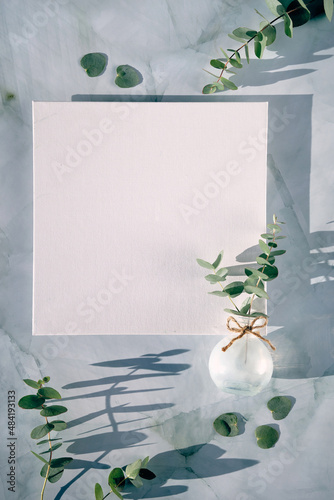 Springtime mockup with blank square canvas and Spring decorations. Fresh eucalyptus twigs in glass vase on mint green stone. Simple monchromatic look. Copy-space, place for your lettering, design. photo