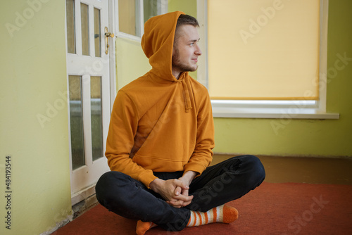 Guy in orange clothes with a hood sits cross-legged on the floor © Tetiana Romaniuk