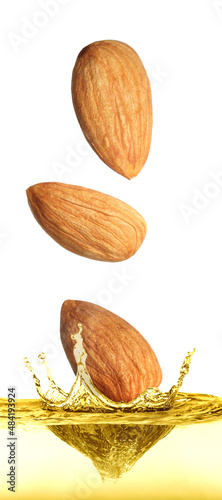 Foto Tasty nuts falling into organic almond oil on white background
