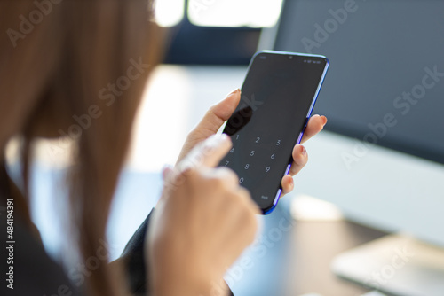 Woman holding a mobile phone using her finger to press the unlock code.