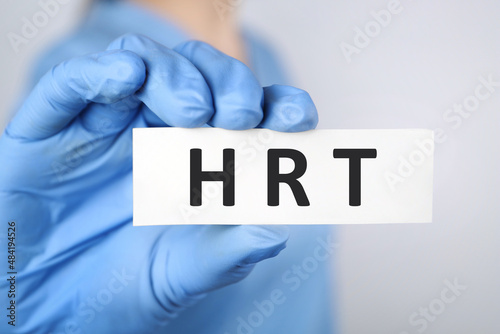 Doctor holding card with abbreviation HRT on light grey background, closeup. Hormone Replacement Therapy photo
