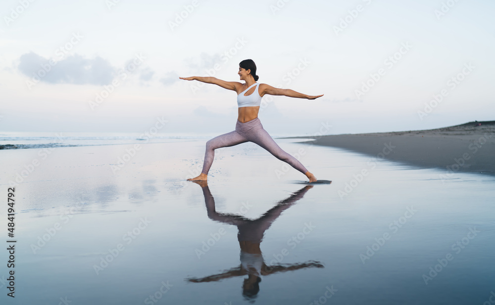 Beautiful female with good looking figure stretching body during morning aerobic exercising at coastline beach, Caucaisan fit girl in tracksuit stretching during warm up workout for feeling vitality Beautiful female with good looking figure stretching body during morning aerobic exercising at coastline beach, Caucaisan fit girl in tracksuit stretching during warm up workout for feeling vitality