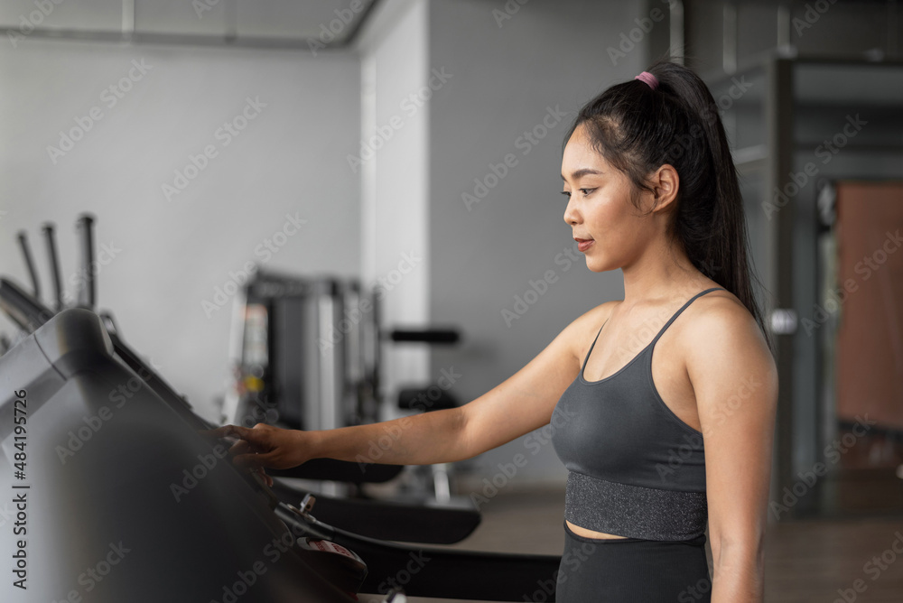 Asian woman exercises in fitness. Young healthy woman in sportswear is running on a treadmill in gym. Asian woman exercises in fitness. Young healthy woman in sportswear is running on a treadmill in gym.