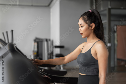 Asian woman exercises in fitness. Young healthy woman in sportswear is running on a treadmill in gym. © sarayutsridee
