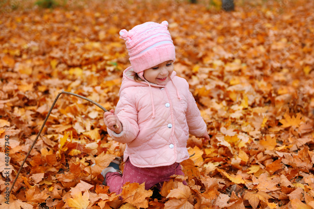 Child girl sitting on fallen leaves in autumn city park. Beautiful nature, trees with yellow leaves. Child girl sitting on fallen leaves in autumn city park. Beautiful nature, trees with yellow leaves.