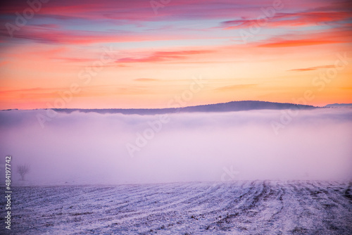 moody winter landscape with fog at sunset