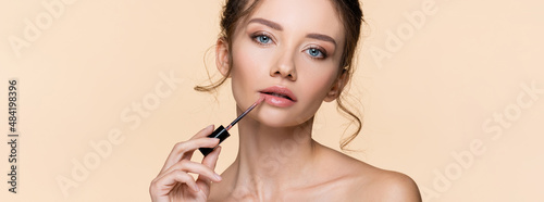 Fotografia Pretty young model applying lip gloss isolated on beige, banner.