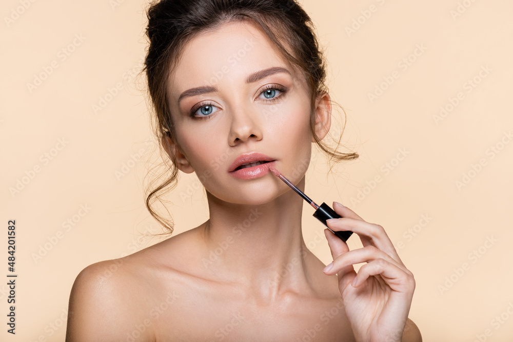 Young woman with naked shoulders applying lip gloss isolated on beige. Young woman with naked shoulders applying lip gloss isolated on beige.