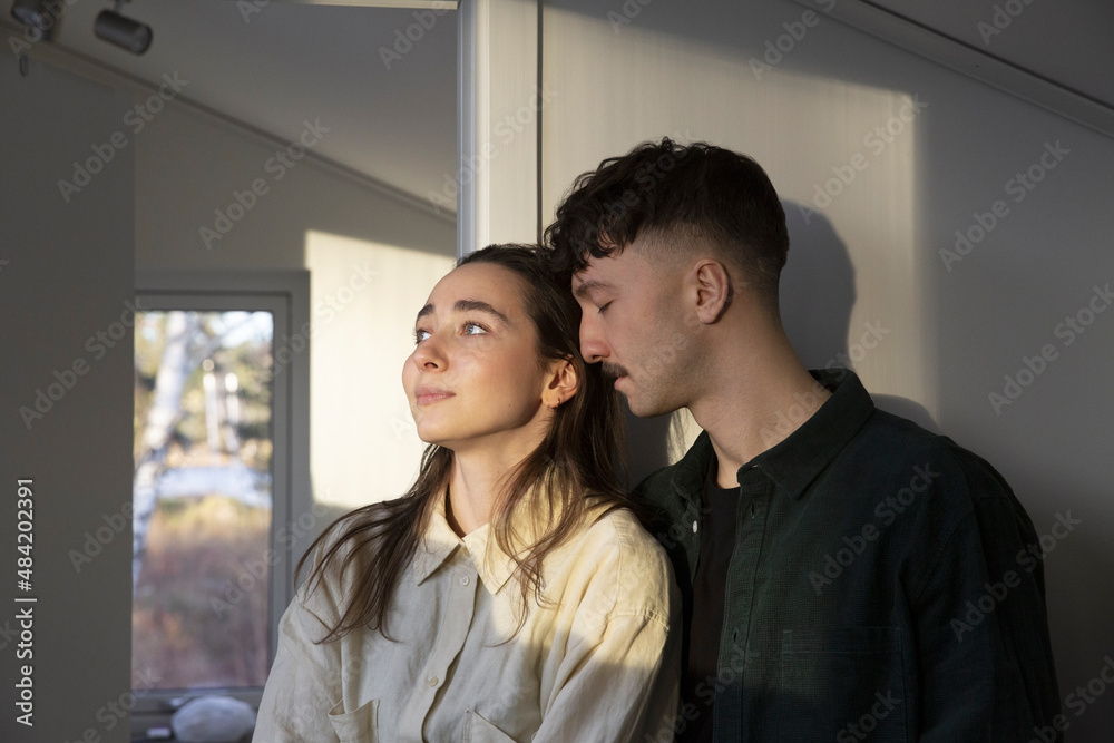 Woman looking away by affectionate boyfriend at home Woman looking away by affectionate boyfriend at home