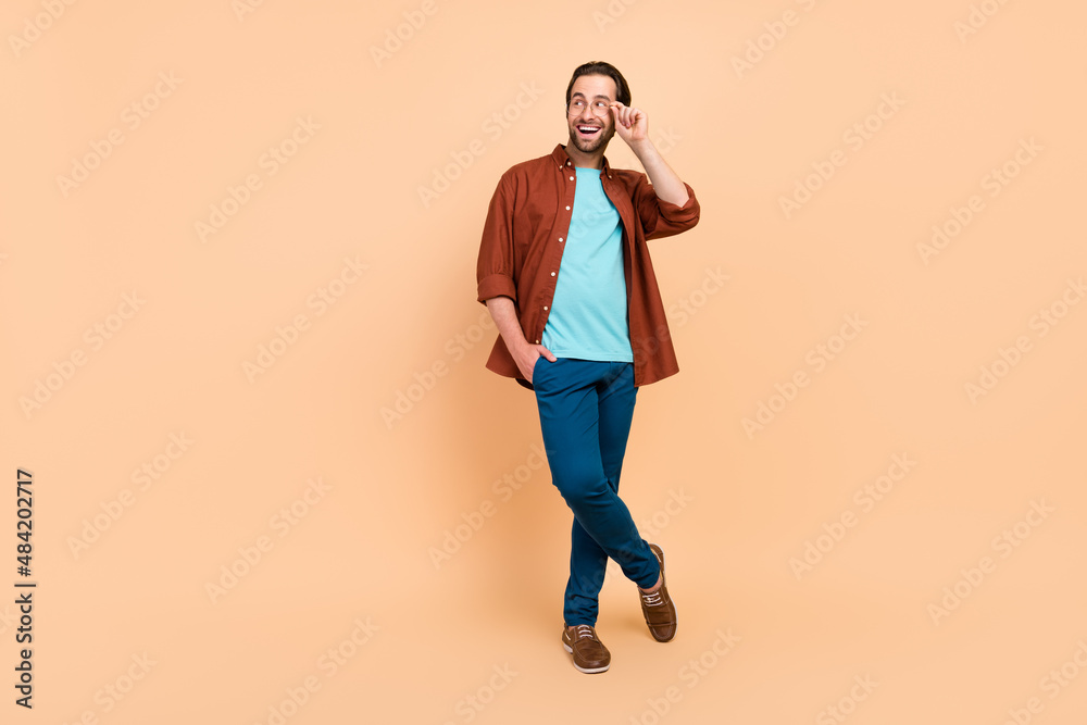 Photo of excited curious funny man look empty space wear specs casual outfit isolated beige color background Photo of excited curious funny man look empty space wear specs casual outfit isolated beige color background