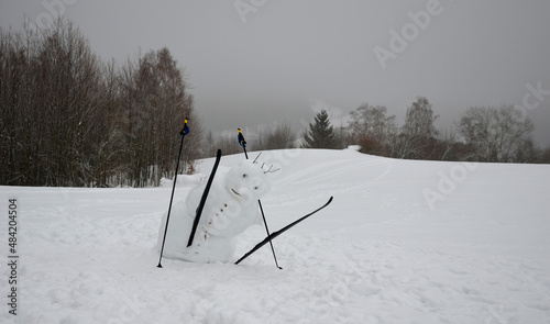 The big snowman has a tilted body that looks like he's falling. has ski poles and cross-country skis. jumping mascot. slow melting and freezing tilts the center of gravity