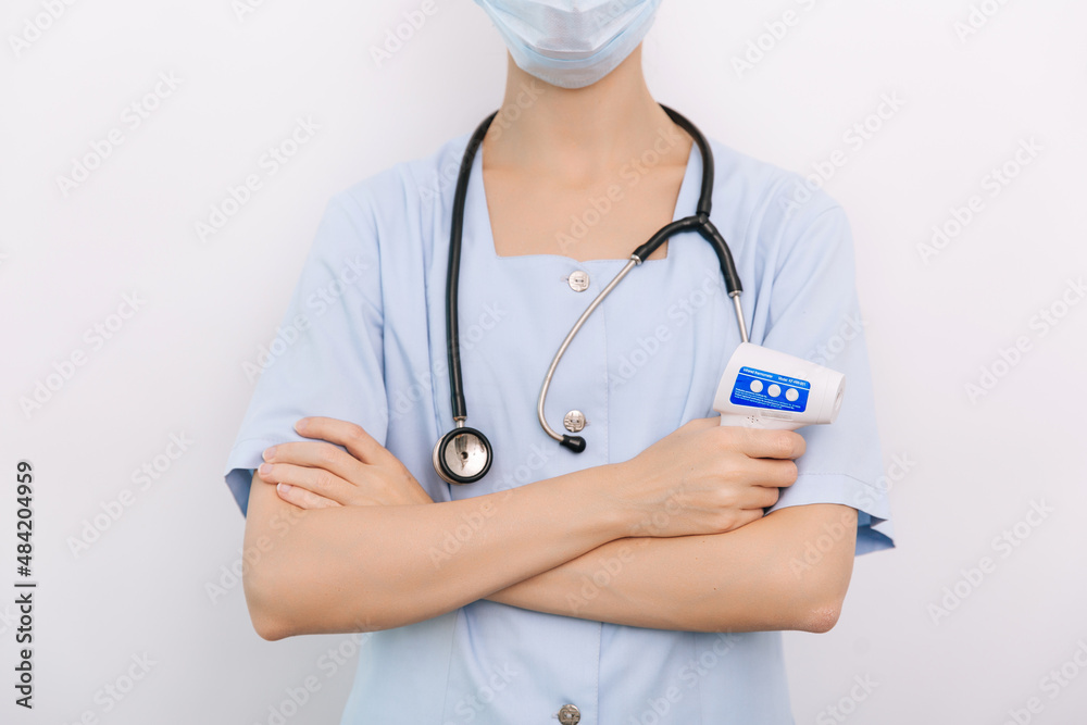 Temperature measurement gun in doctor hands. Close-up shot of doctor wearing protective surgical mask ready to use infrared isometric thermometer gun to check body temperature for virus symptoms Temperature measurement gun in doctor hands. Close-up shot of doctor wearing protective surgical mask ready to use infrared isometric thermometer gun to check body temperature for virus symptoms