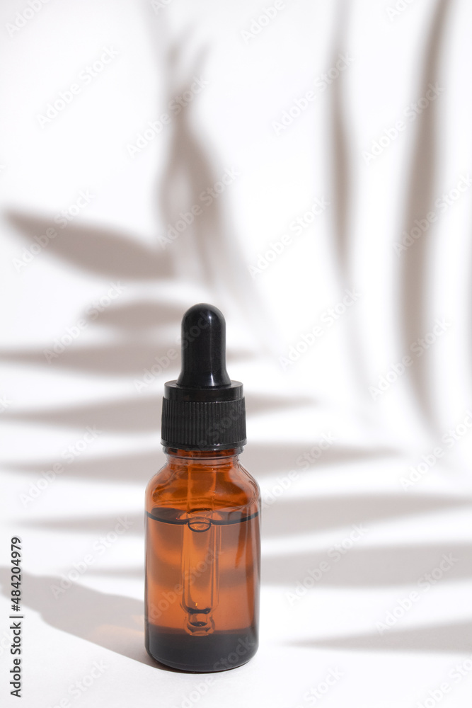 Glass dropper bottle with shadow palm leaves. Cosmetic container mock-up. Creative minimalistic shot of a cosmetic product. Spa concept. Mock-up bottle for branding and label