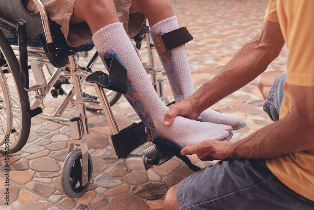 Obraz premium Parent helping wear protective equipment to prevent foot injuries to young man with a disability, Shoes to support foot deformities in people with disabilities and medical equipments concept.