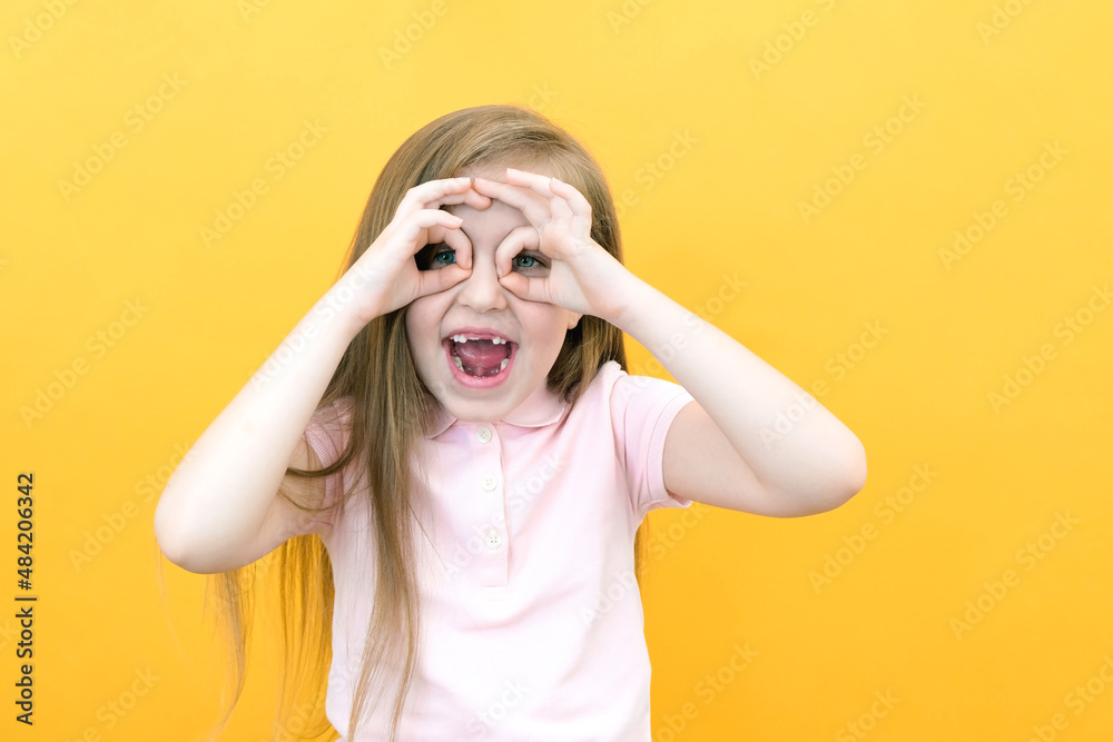 Fun, joy, relaxation and happy childhood. a little girl in a casual t-shirt makes a mask, keeps her hands near her eyes Fun, joy, relaxation and happy childhood. a little girl in a casual t-shirt makes a mask, keeps her hands near her eyes