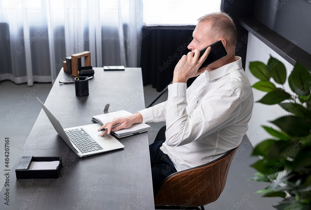 Mature man sitting at desk with laptop and planner. Businessman speaking on phone with colleague or business partner. Business call concept. High quality photo Mature man sitting at desk with laptop and planner. Businessman speaking on phone with colleague or business partner. Business call concept. High quality photo