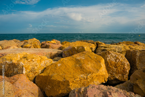 Big stones of breakwater by the sea, blue sky clouds