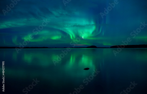 Northern lights dancing over calm lake in Farnebofjarden national park in north of Sweden.