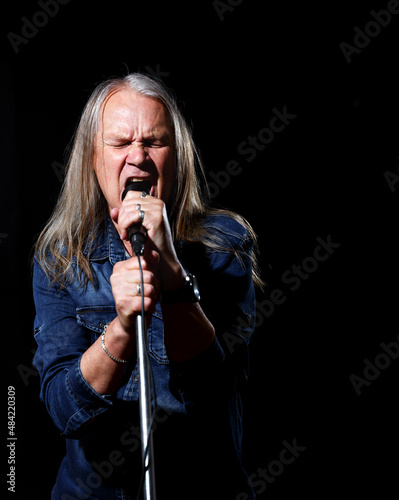 elderly man with long gray hair sings into a microphone