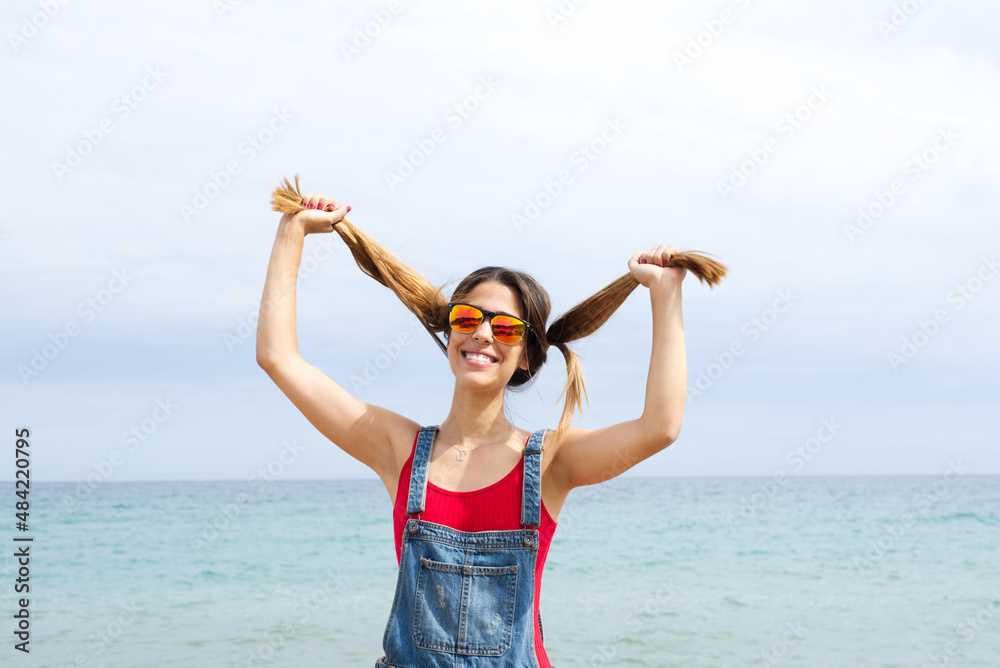 Jovial girl in sunglasses holds her pigtails with her hands on the beach in summer with expression of happiness. Jovial girl in sunglasses holds her pigtails with her hands on the beach in summer with expression of happiness.