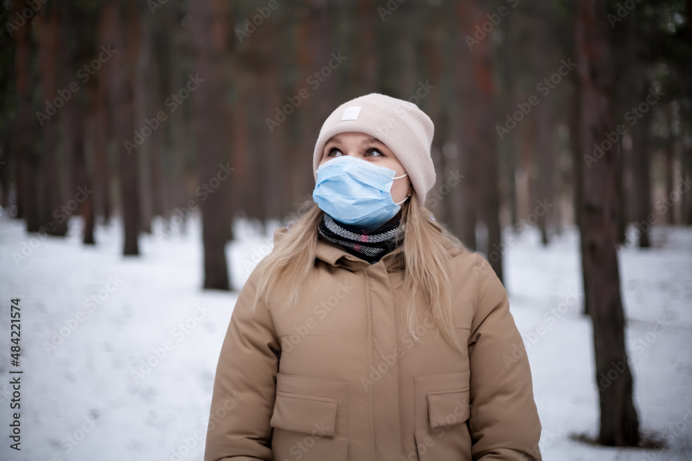 Obraz premium Attractive blonde girl in a medical mask is walking in the forest.