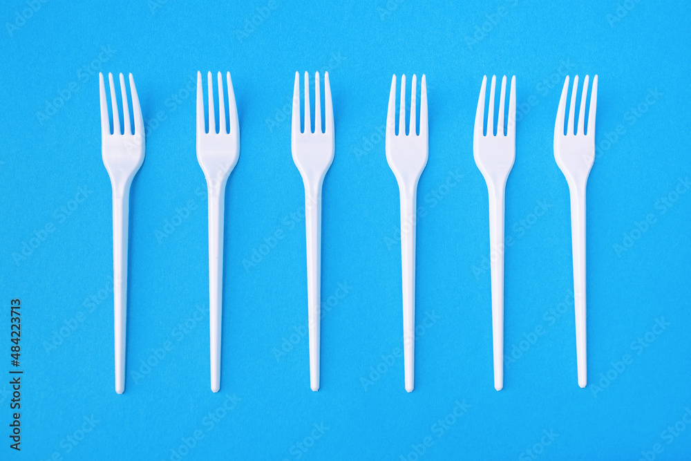 Six plastic forks on a blue paper background for single use. Dangerous plastic for the environment. Disposable eating utensils Six plastic forks on a blue paper background for single use. Dangerous plastic for the environment. Disposable eating utensils