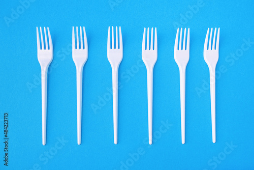 Six plastic forks on a blue paper background for single use. Dangerous plastic for the environment. Disposable eating utensils