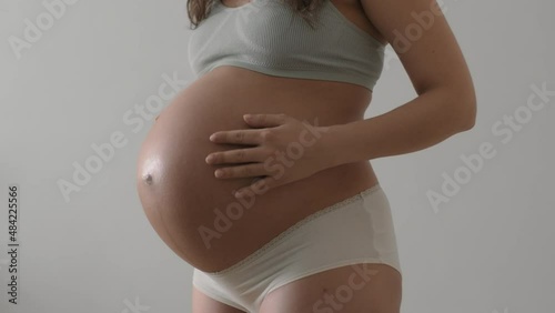 Close-up of pregnant belly of expectant mother wearing underwear on white background. Young woman is waiting for a baby, gently and tenderly stroking her stomach