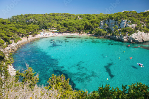View over the turquoise waters of Cala Macarella to pine-fringed sandy beach, Cala Galdana, Menorca, Balearic Islands photo