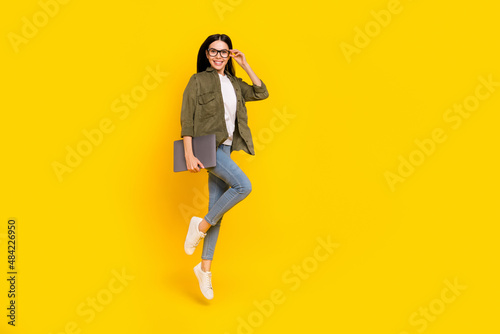 Full size photo of funny young lady jump hold laptop wear eyewear shirt jeans footwear isolated on yellow background