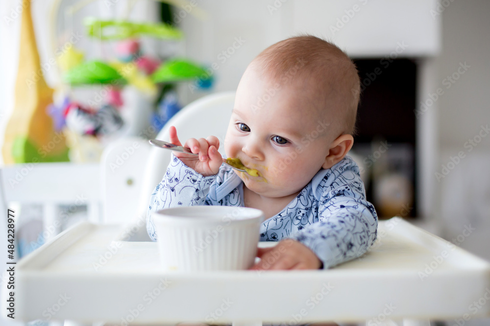 Cute little baby boy, eating mashed vegetables for lunch, mom feeding him Cute little baby boy, eating mashed vegetables for lunch, mom feeding him