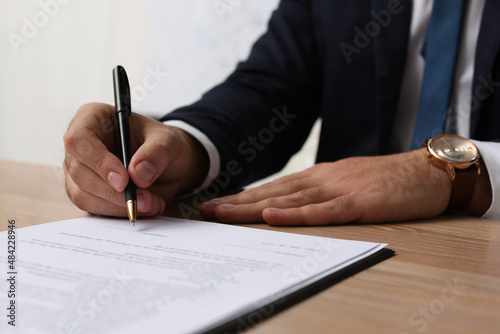 Businessman signing contract at wooden table indoors, closeup