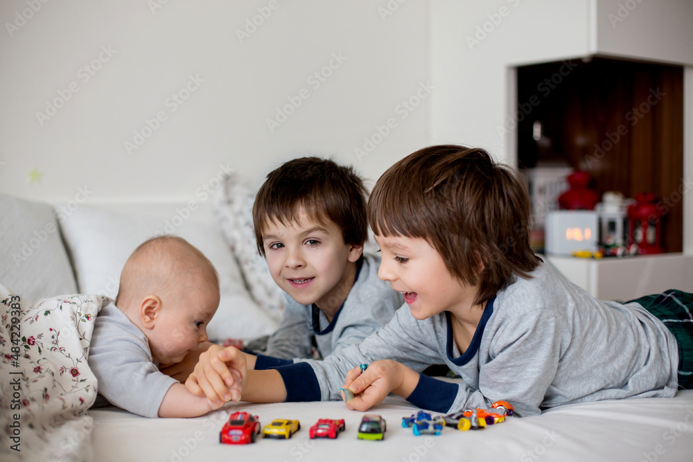 Three children, baby and his older brothers in bed in the morning, playing together Three children, baby and his older brothers in bed in the morning, playing together