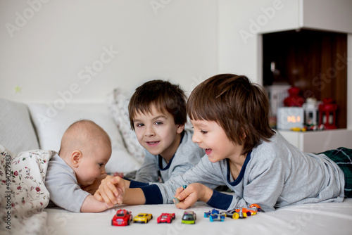 Three children, baby and his older brothers in bed in the morning, playing together