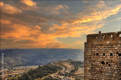 Vista desde lo alto de un valle en España con un camino descendente. Un atardecer de nubes rojizas y al costado una alta pared de piedras con la cabeza sobresaliente de una persona no identificable. photo