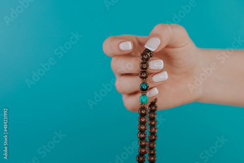 Woman lit hand counts mala beads strands of gemstones used for keeping count during mantra meditations. Blue background. Spirituality, religion, God concept.