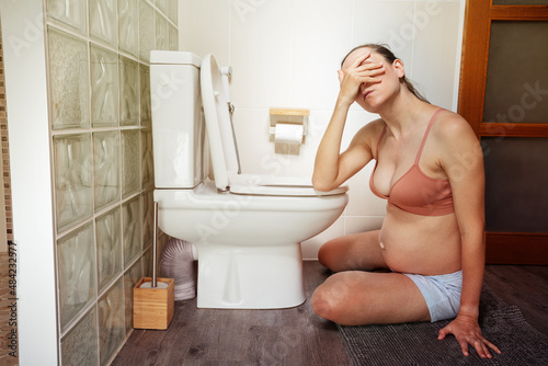 Tired pregnant woman sit on the floor in toilet