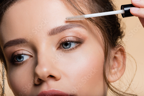 Quadro em tela Cropped view of young woman applying eyebrow gel isolated on beige
