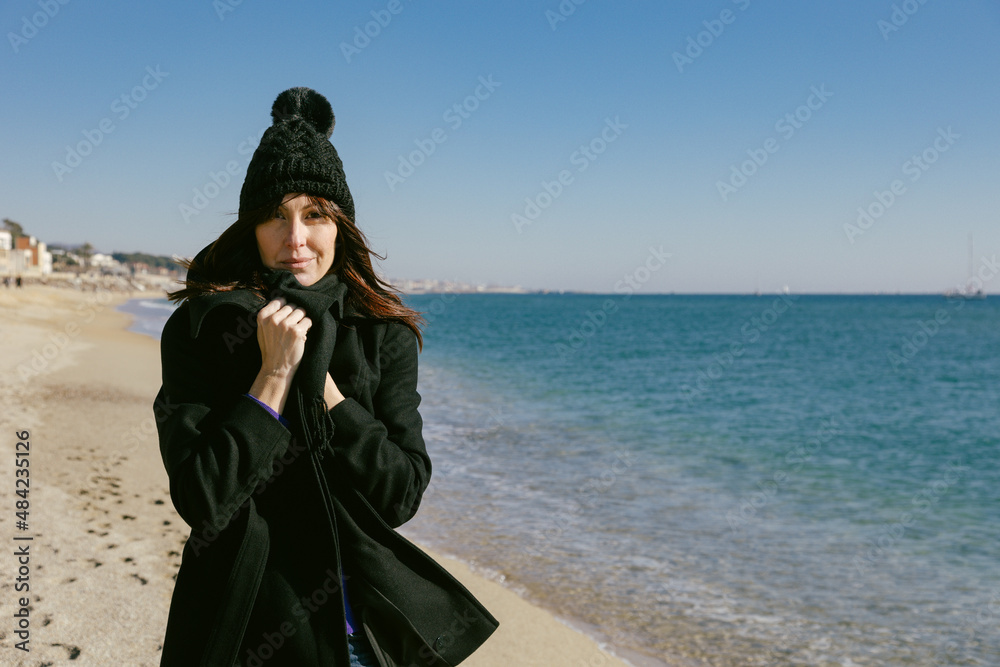 Woman with hat and coat on the beach on a sunny winter day Woman with hat and coat on the beach on a sunny winter day