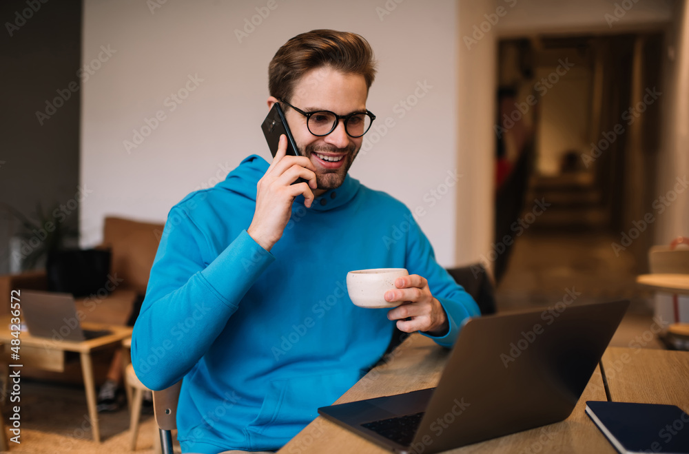 Smiling hipster guy editing content vlog on laptop computer calling to influence colleague for discussing ideas, happy millennial freelancer using cellular for phoning and netbook for networking Smiling hipster guy editing content vlog on laptop computer calling to influence colleague for discussing ideas, happy millennial freelancer using cellular for phoning and netbook for networking