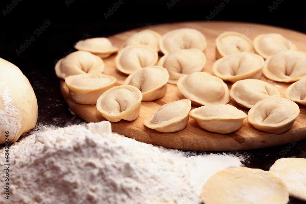 Raw meat dumplings and flour on dark background close-up. Traditional Russian pelmeni. Selective focus. Raw meat dumplings and flour on dark background close-up. Traditional Russian pelmeni. Selective focus.