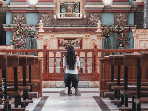 latina girl kneeling in front of the altar of an old church demonstrating her devotion selective focus © Renato