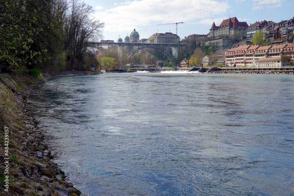 River Aare in Bern with city skyline on the background. There are historic buildings on along the riverbank and Swiss federal assembly representing swiss parliament. 